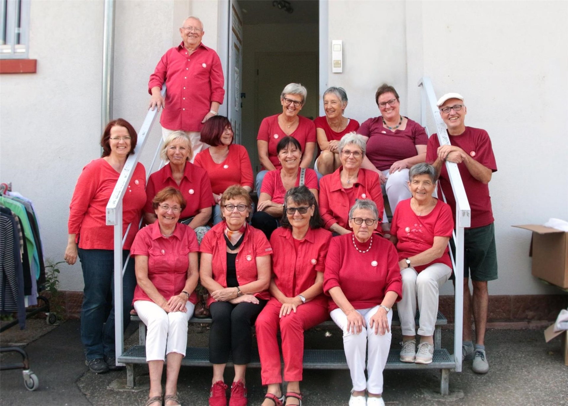 13 Frauen und 2 Männer, alle in roten Oberteilen, sitzen bzw. stehen auf einer Treppe